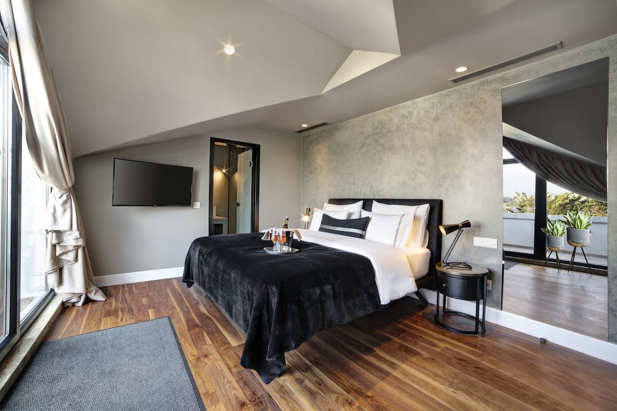 A modern bedroom with a large bed, a flat-screen TV, a small side table, and a view of the outdoors.