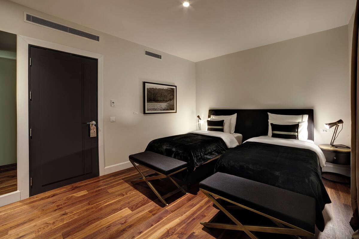 A bedroom with two beds, a bench, a bedside table, a lamp, and a picture on the wall.