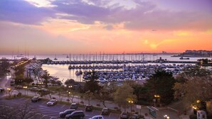 Uma marina com barcos atracados, um estacionamento e um pôr do sol sobre a água.