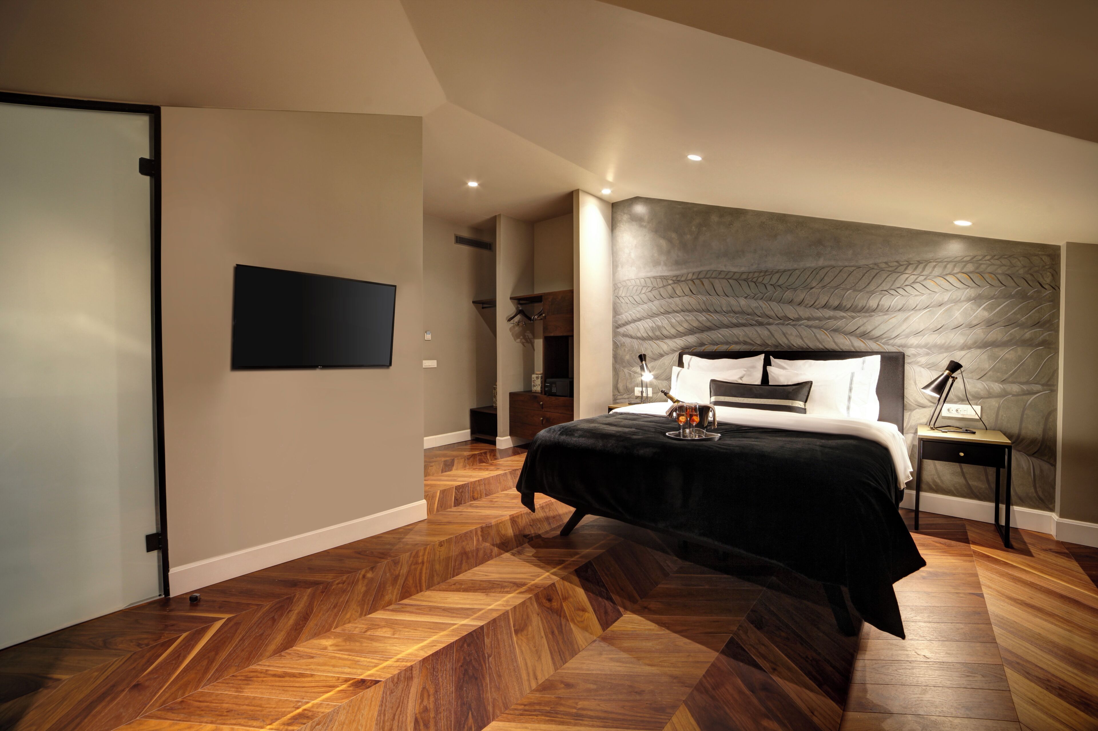 A modern bedroom with a large bed, a flat-screen TV mounted on the wall, and a unique textured wall design.
