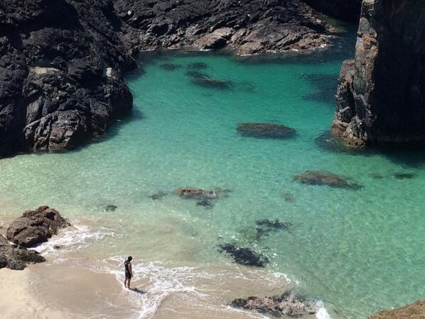 Paesaggio costiero con acque turchesi cristalline, formazioni rocciose e una persona in spiaggia.