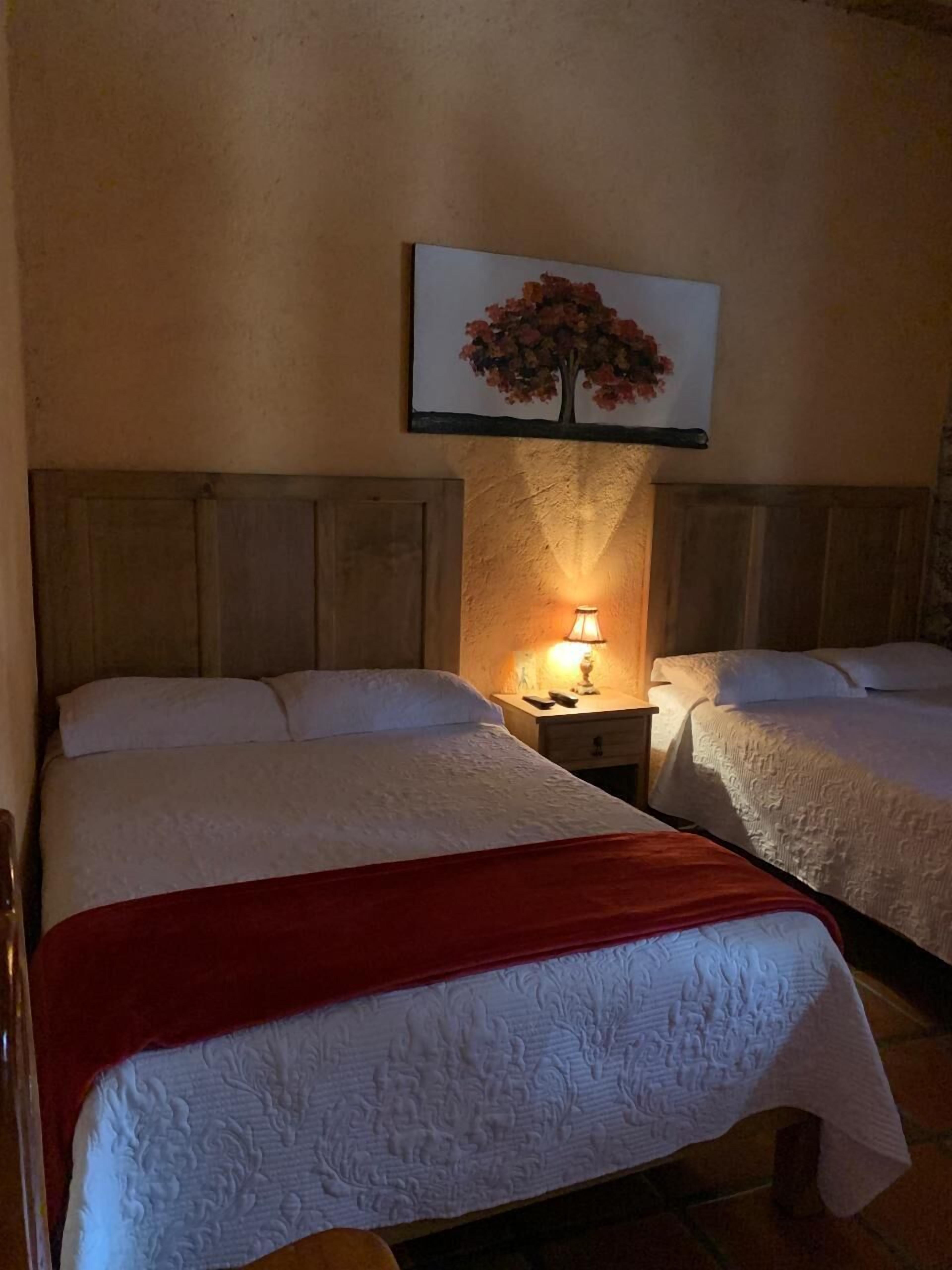 Ett hotellrum med två sängar, en sänggavel i trä, ett nattduksbord med en lampa och en inramad tavla på väggen.