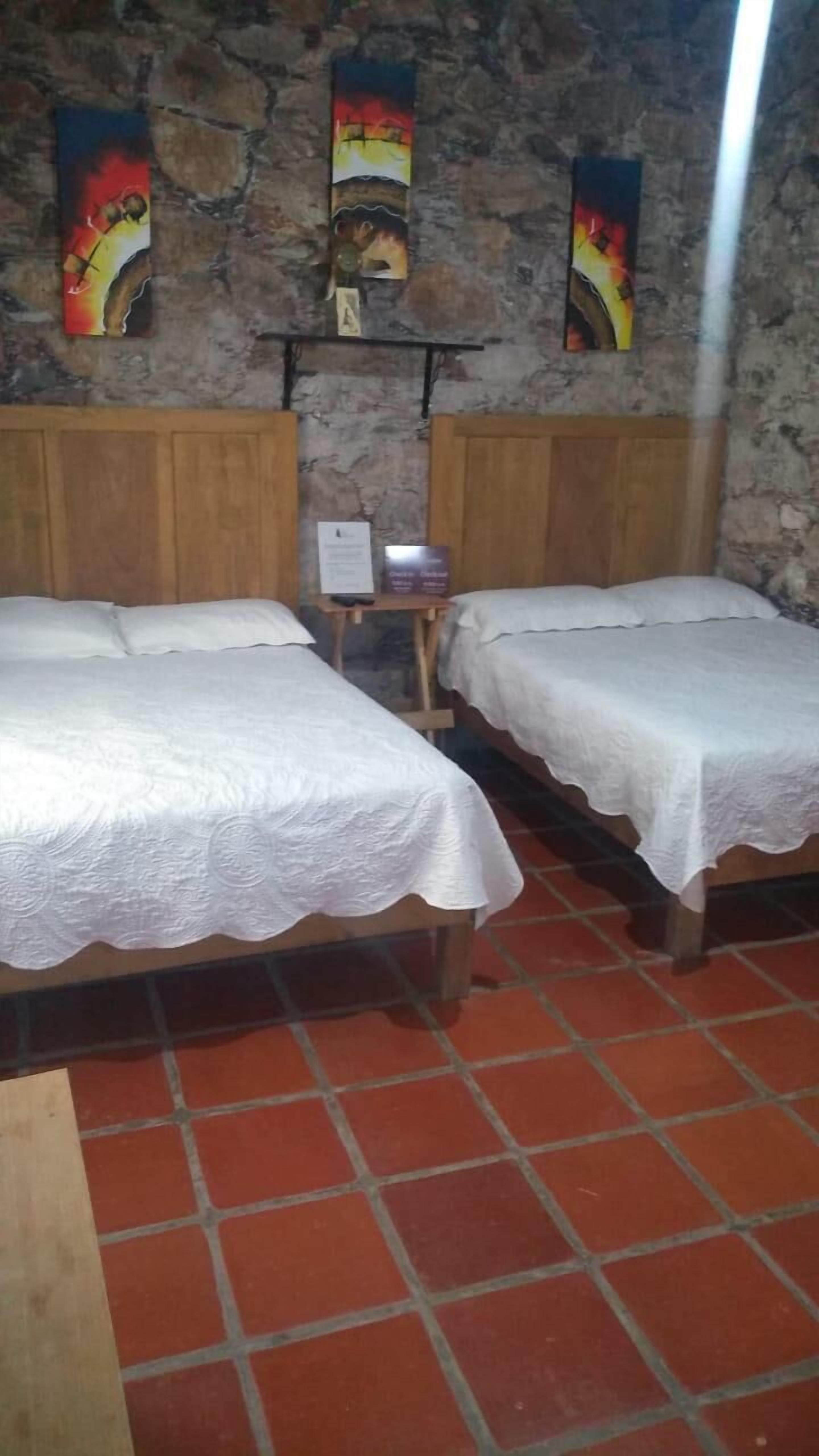 Two single beds with white linens in a room with a stone wall and a tiled floor.