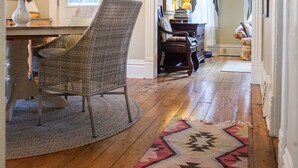 Un pasillo con piso de madera, alfombra estampada, sillas de mimbre, una lámpara y un candelabro.