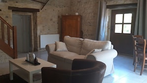 A living room with a sofa, a coffee table, a wooden chair, a cabinet, and a staircase. - Charming cottage with a veranda facing south overlooking an orchard. (Colleville-sur-Mer)