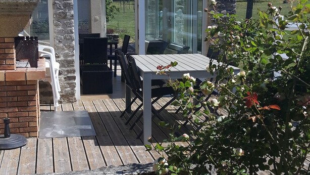 A patio with a table and chairs, a stone wall, and a view of the garden. - Charming cottage with a veranda facing south overlooking an orchard. (Colleville-sur-Mer)