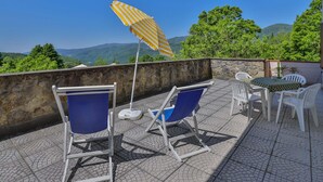 Une terrasse avec des sièges extérieurs, un mur en pierre et une vue sur des collines verdoyantes.