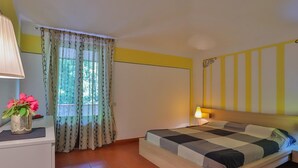 A bedroom with a bed, a bedside table with a lamp, a window with curtains, and a vase with flowers. - Residence a Pistoia ID 3781 (Pistoia)