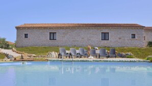 Un bâtiment en pierre avec un toit en tuiles, une piscine et plusieurs chaises longues.