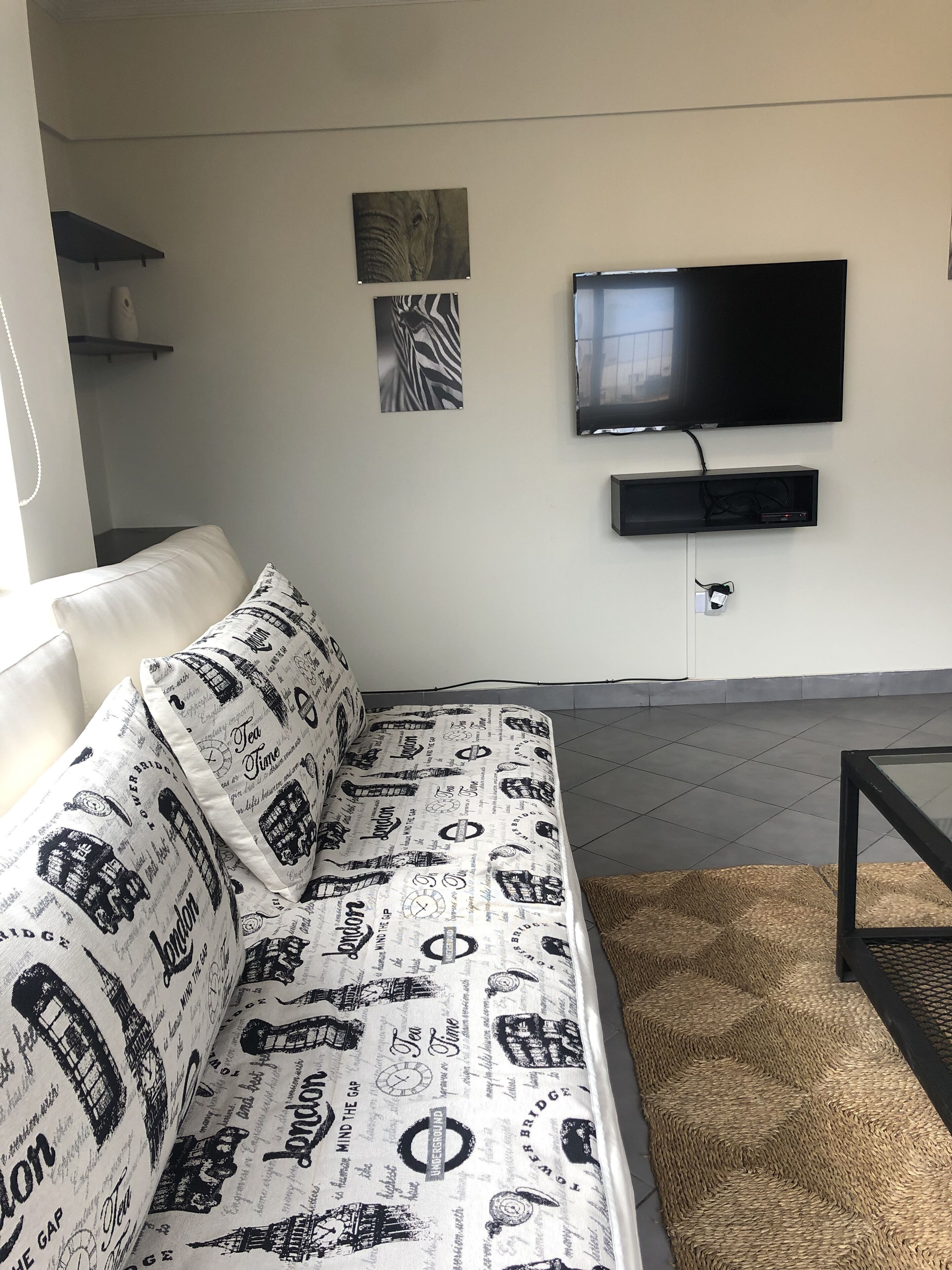 A living room with a sofa, a flat-screen TV mounted on the wall, and a woven rug on the floor.
