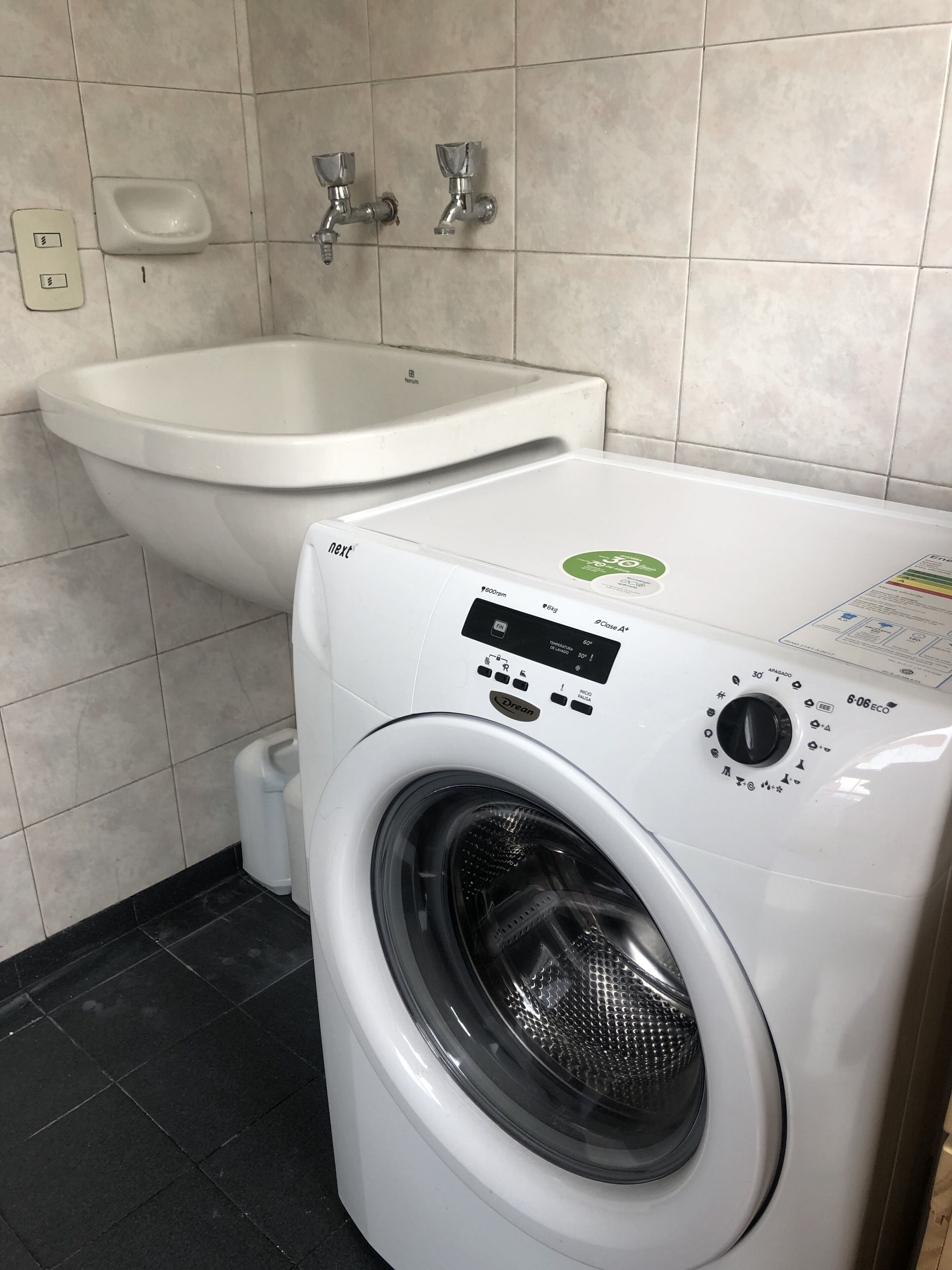 A front-loading washing machine with a control panel, a white sink, and a toilet in a bathroom.