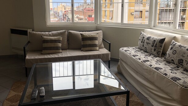 A modern living room with a sofa, a glass coffee table, and a view of a cityscape through large windows. - Amplio & Luminoso Depto Centro de Salta (Salta)