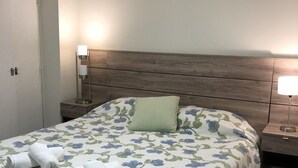 A neatly made bed with floral bedding, a wooden headboard, and bedside lamps. - Amplio & Luminoso Depto Centro de Salta (Salta)