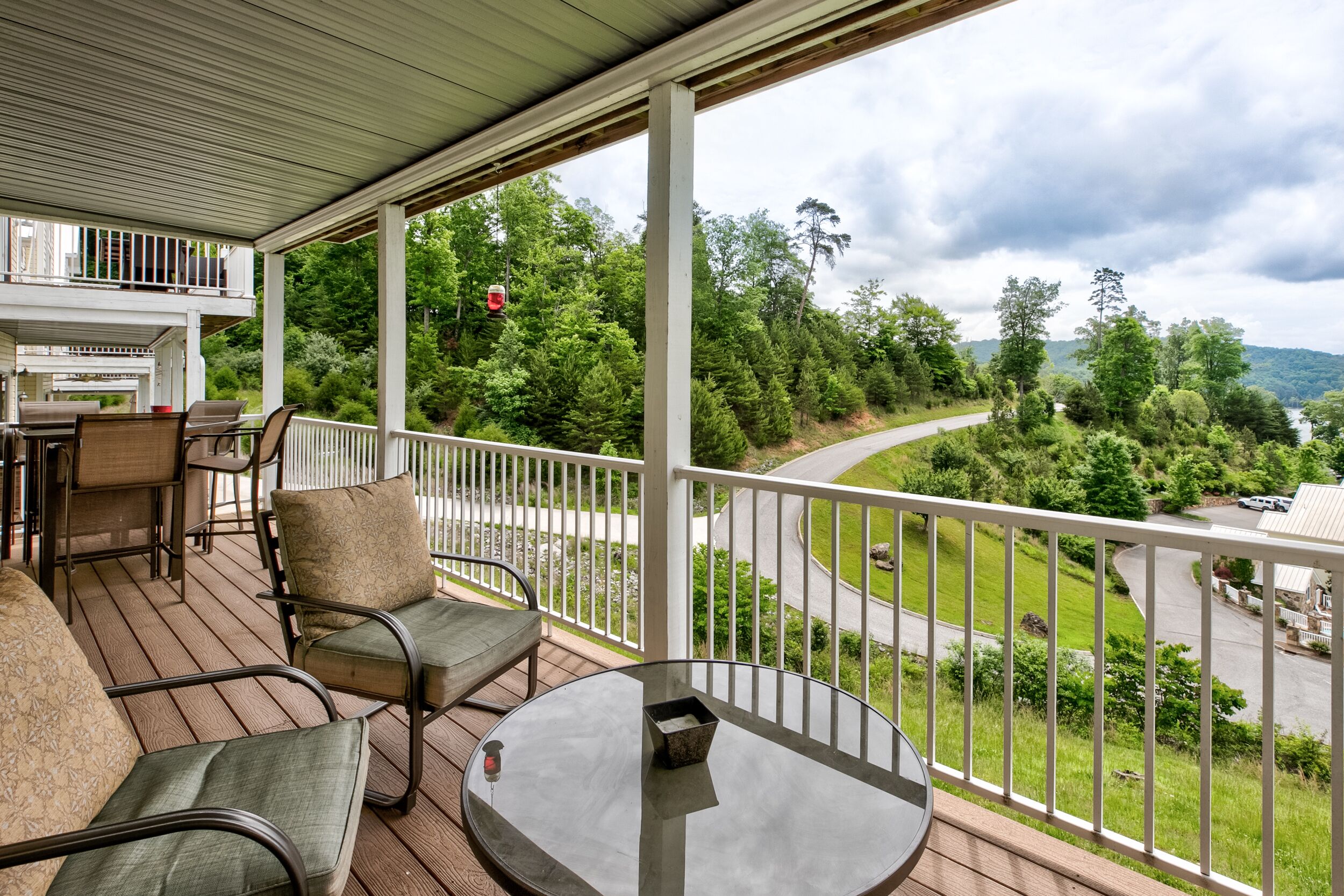 A covered outdoor area with a table and chairs, overlooking a road and greenery.