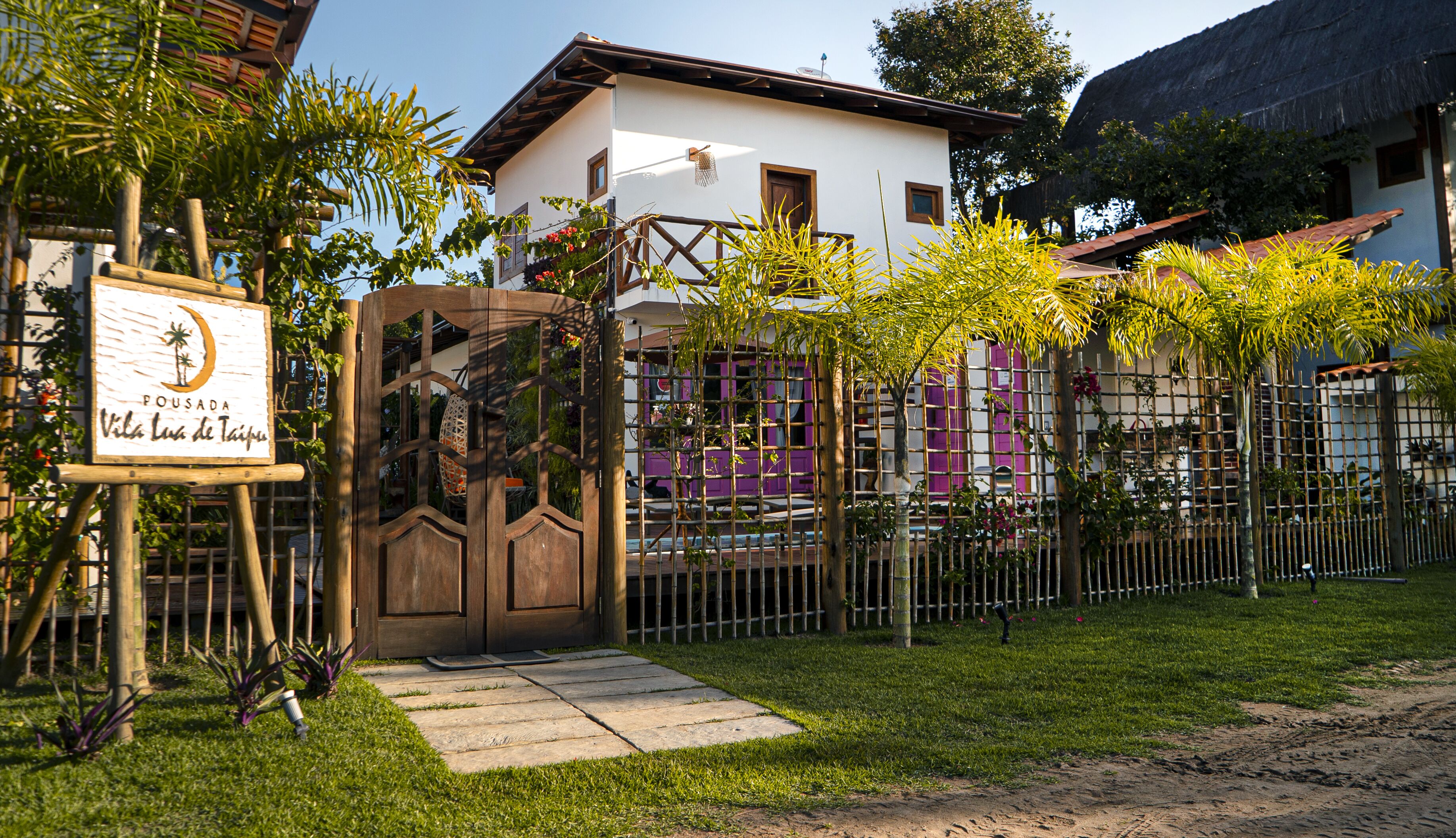 A villa with a wooden gate, a signboard, and a fenced garden area.