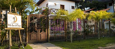 A villa with a wooden gate, a signboard, and a fenced garden area.