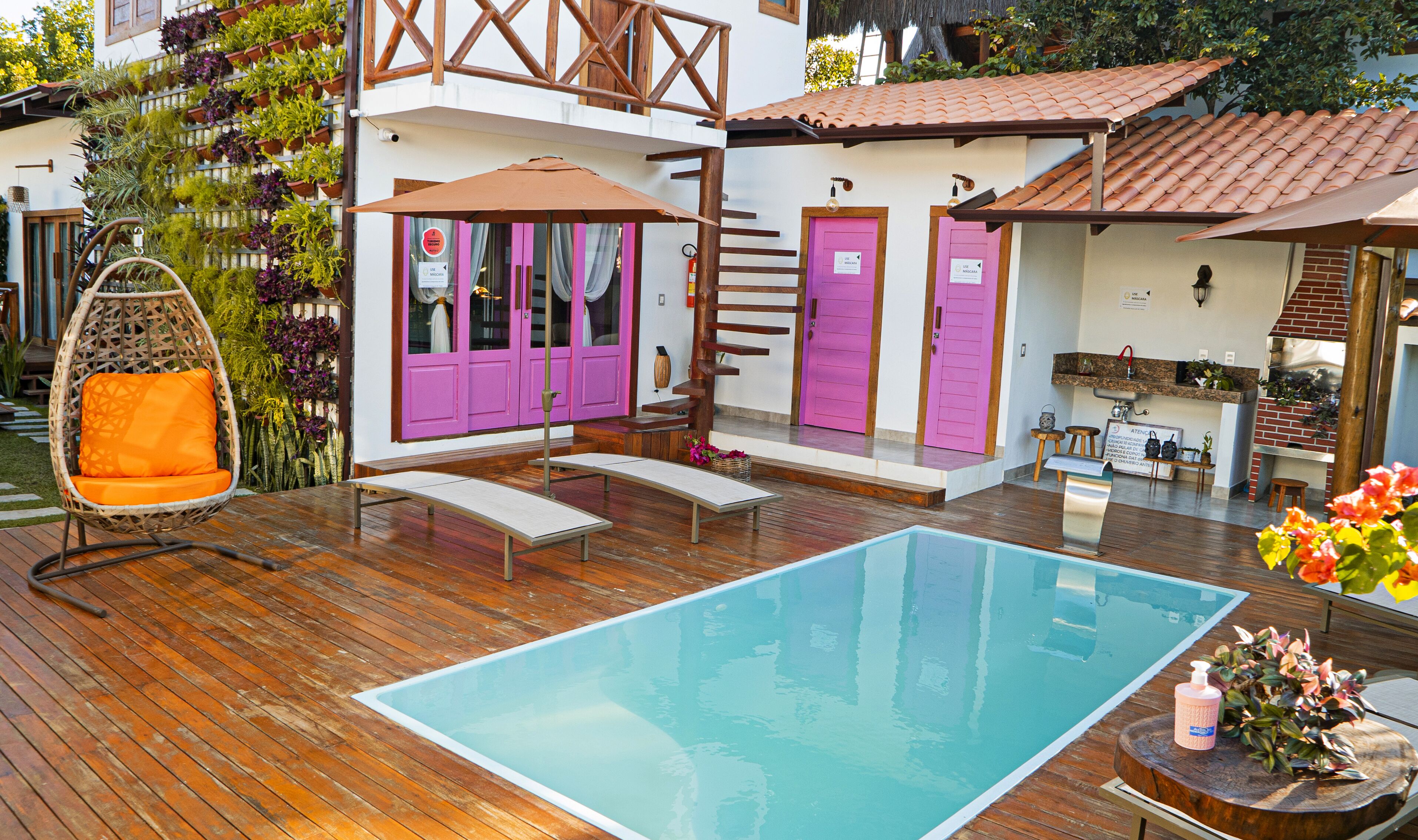 A pool area with wooden decking, a hanging chair, and a small table with a bottle.