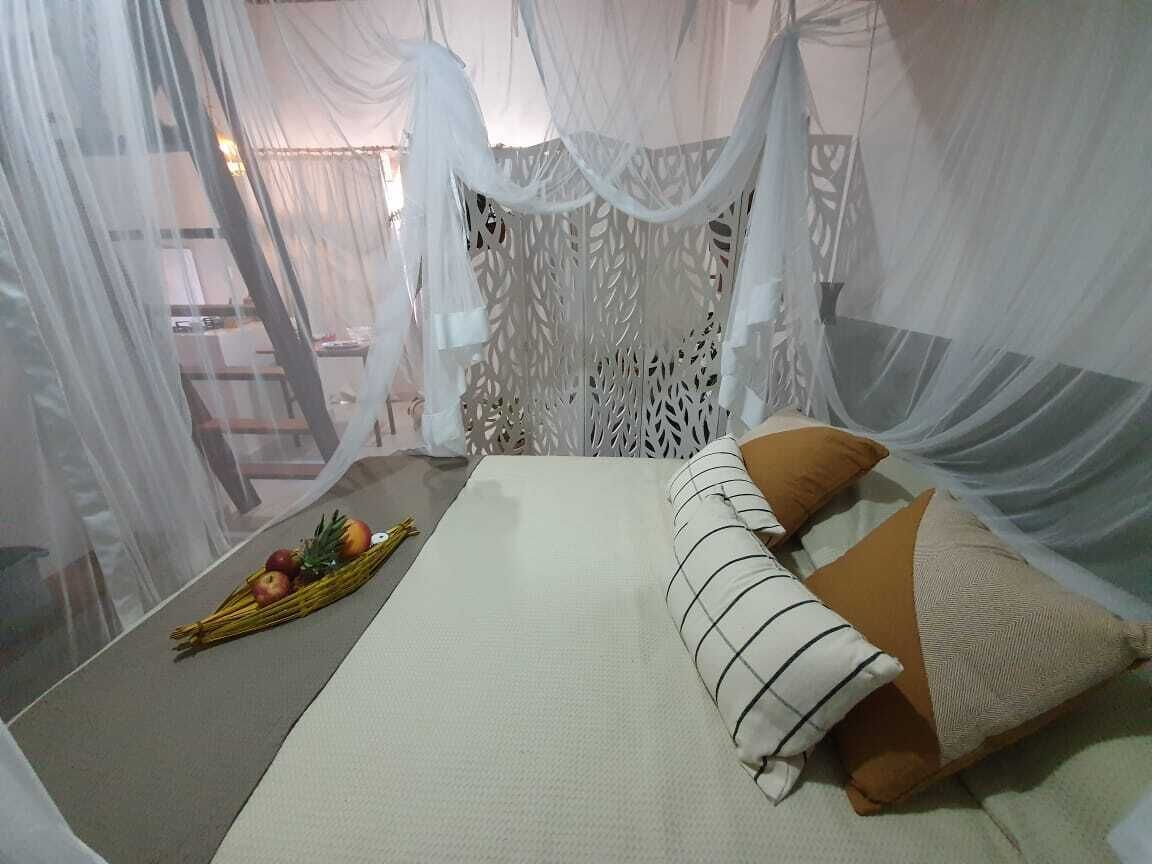 A bed with a canopy, pillows, and a fruit arrangement on the floor.