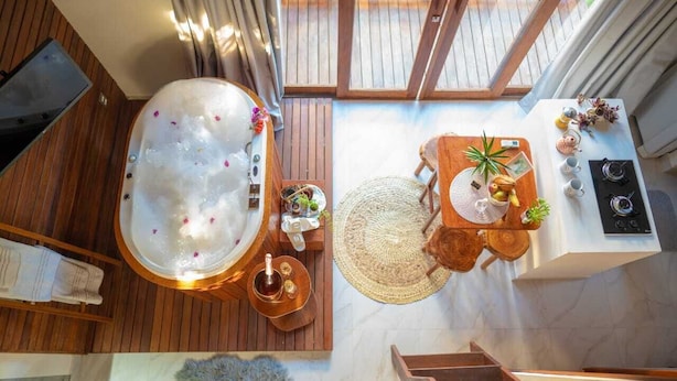 Ein Spa-Raum mit einer großen Whirlwanne, Holzboden, einem kleinen Tisch mit Früchten und einer Pflanze sowie Blick ins Freie.