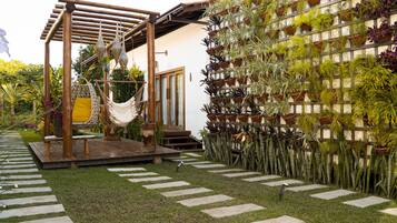 Un jardín con una pérgola de madera, una silla colgante y un muro de plantas en macetas.