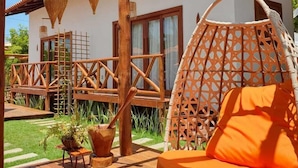 Eine Holzterrasse mit einem hängenden orangefarbenen Stuhl, einer Holzpergola und einem weißen Gebäude mit Fenstern und einer Tür.