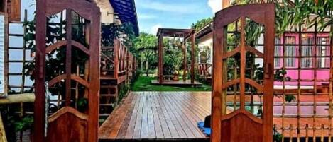 A wooden pathway leading to a covered area with a pergola and a small deck.