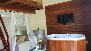 Ein Schlafzimmer mit Himmelsbett, Holzofen-Whirlpool, an einer Holzwand montiertem Fernseher und einem kleinen Hocker.