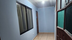 Un couloir avec un sol carrelé, une porte et une fenêtre avec des rideaux.