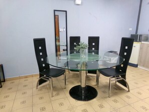 Un coin repas comprenant une table ronde en verre, quatre chaises noires, une petite plante en pot et un miroir accroché au mur.