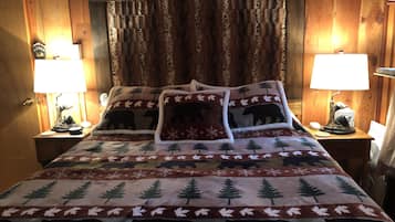 Una habitación acogedora con paneles de madera, una cama con manta temática de oso, dos lámparas de noche y una mesita con lámpara y adorno.