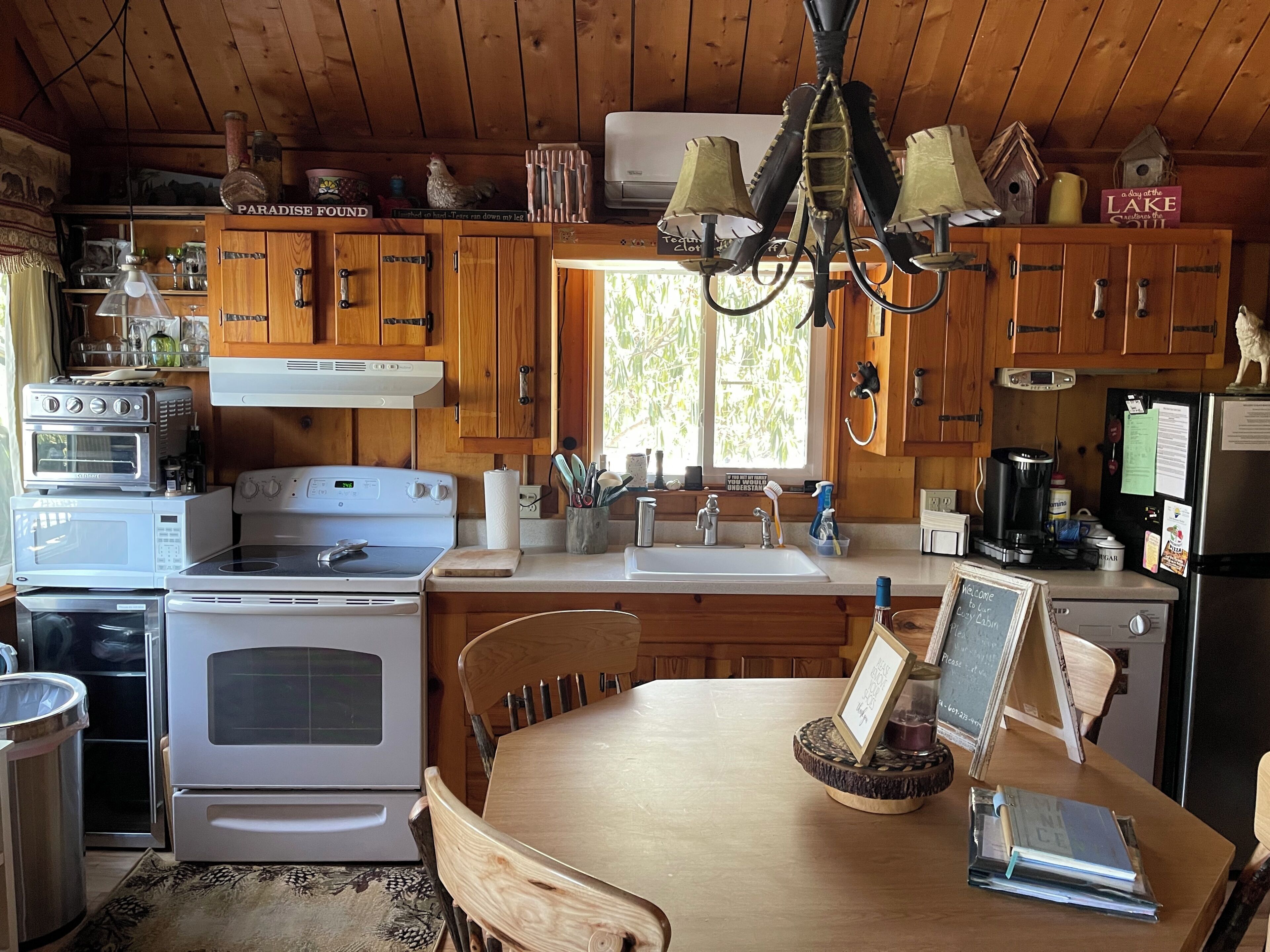 A cabin kitchen with wooden cabinets, a stove, a sink, and a dining area with a table and chairs.