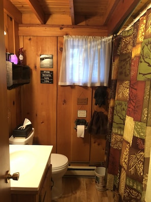 A wooden cabin bathroom with a toilet, sink, and a shower curtain with a leaf pattern.
