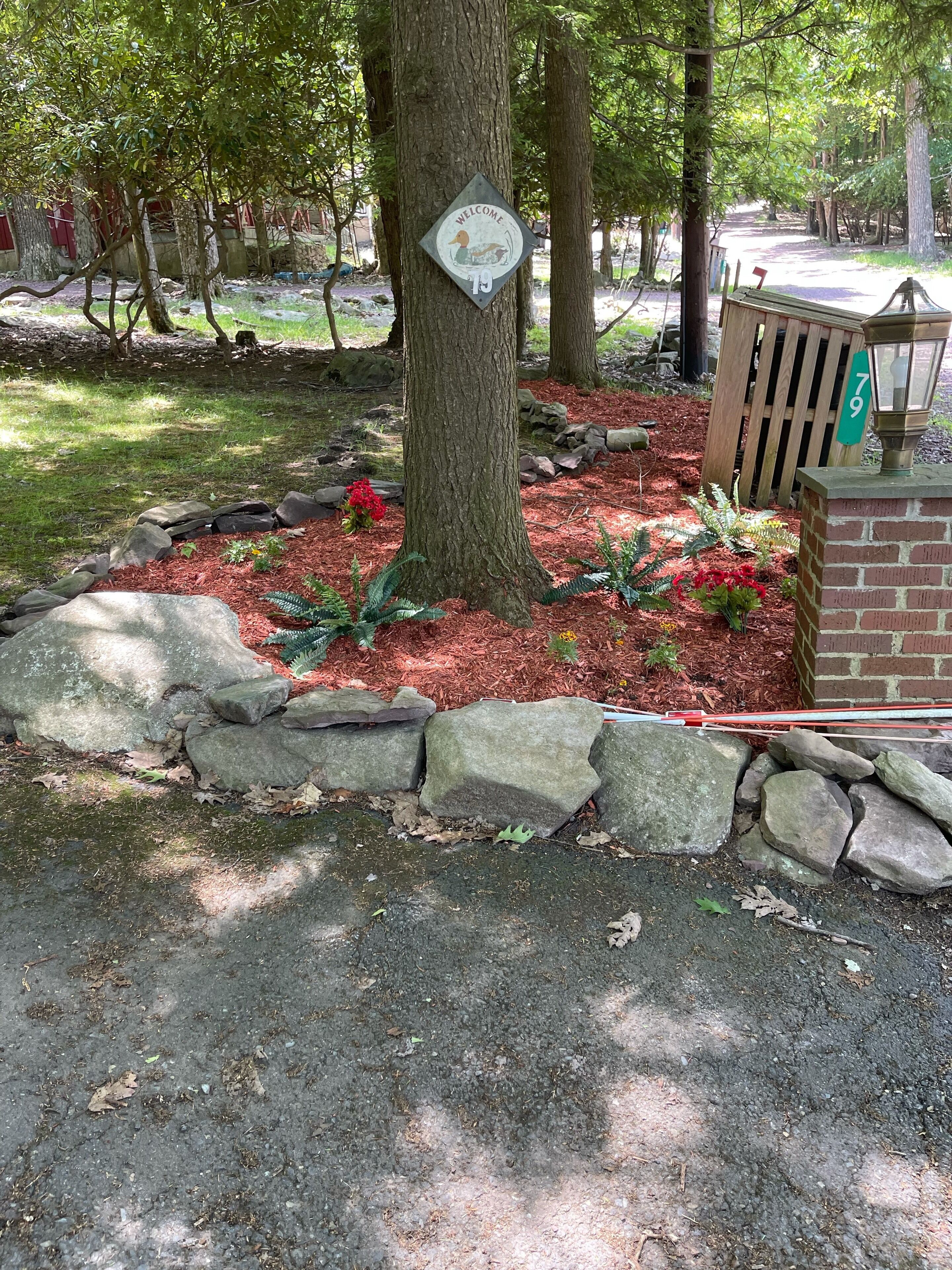 A landscaped garden area with a welcome sign, a brick wall, and a wooden fence.