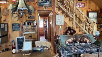 A cabin interior with a wooden staircase, a couch with animal prints, and various signs and decorations.