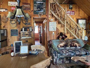 A cabin interior with a wooden staircase, a couch with animal prints, and various signs and decorations.