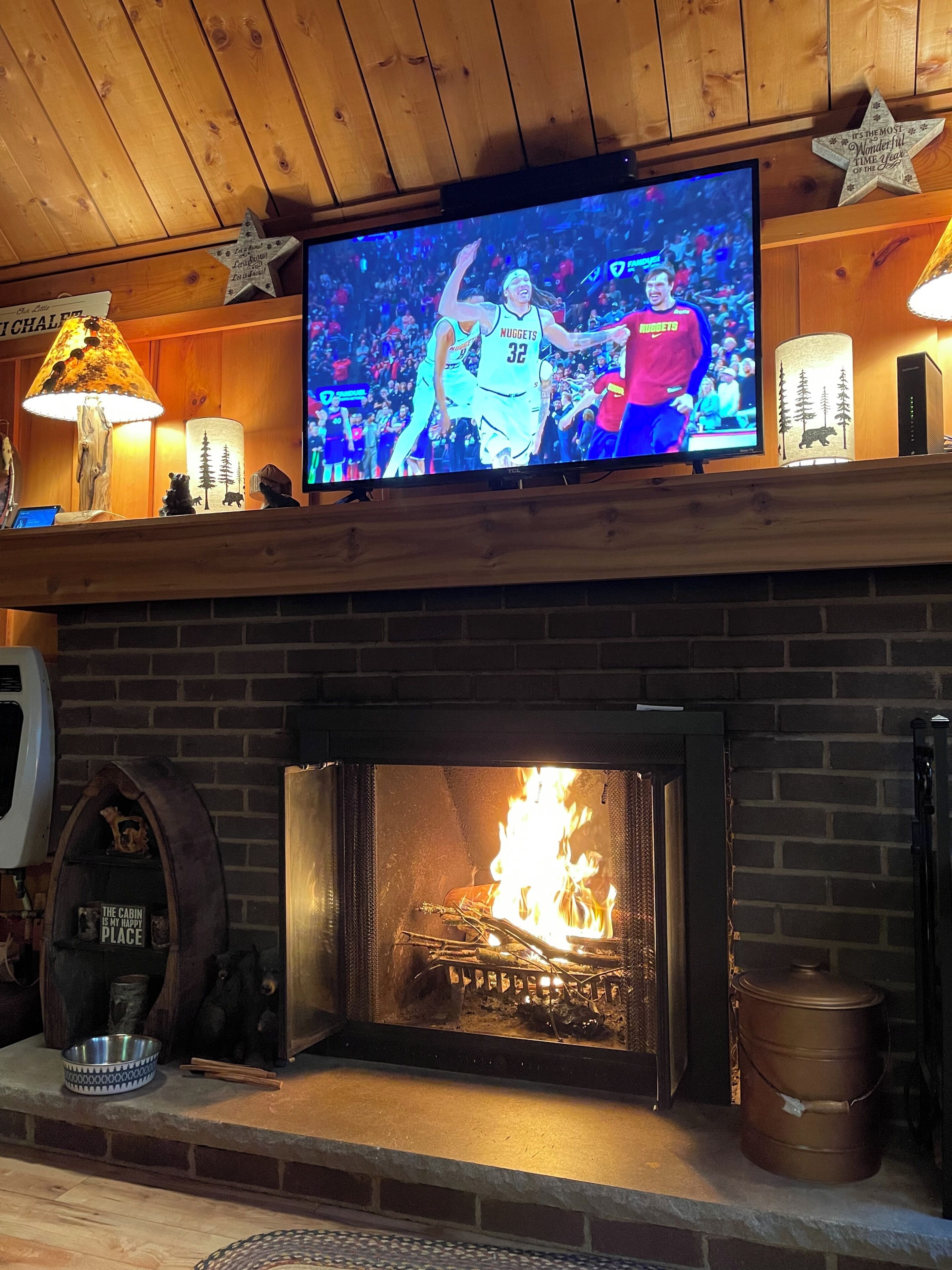 A fireplace with a TV mounted above it, displaying a basketball game.