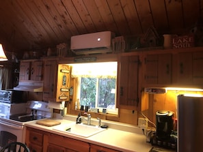 A kitchen with wooden cabinets, a stove, a sink, and a window with a view of greenery.