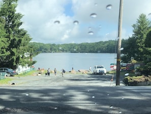A view of a lake with a road leading to it, surrounded by trees and parked vehicles.