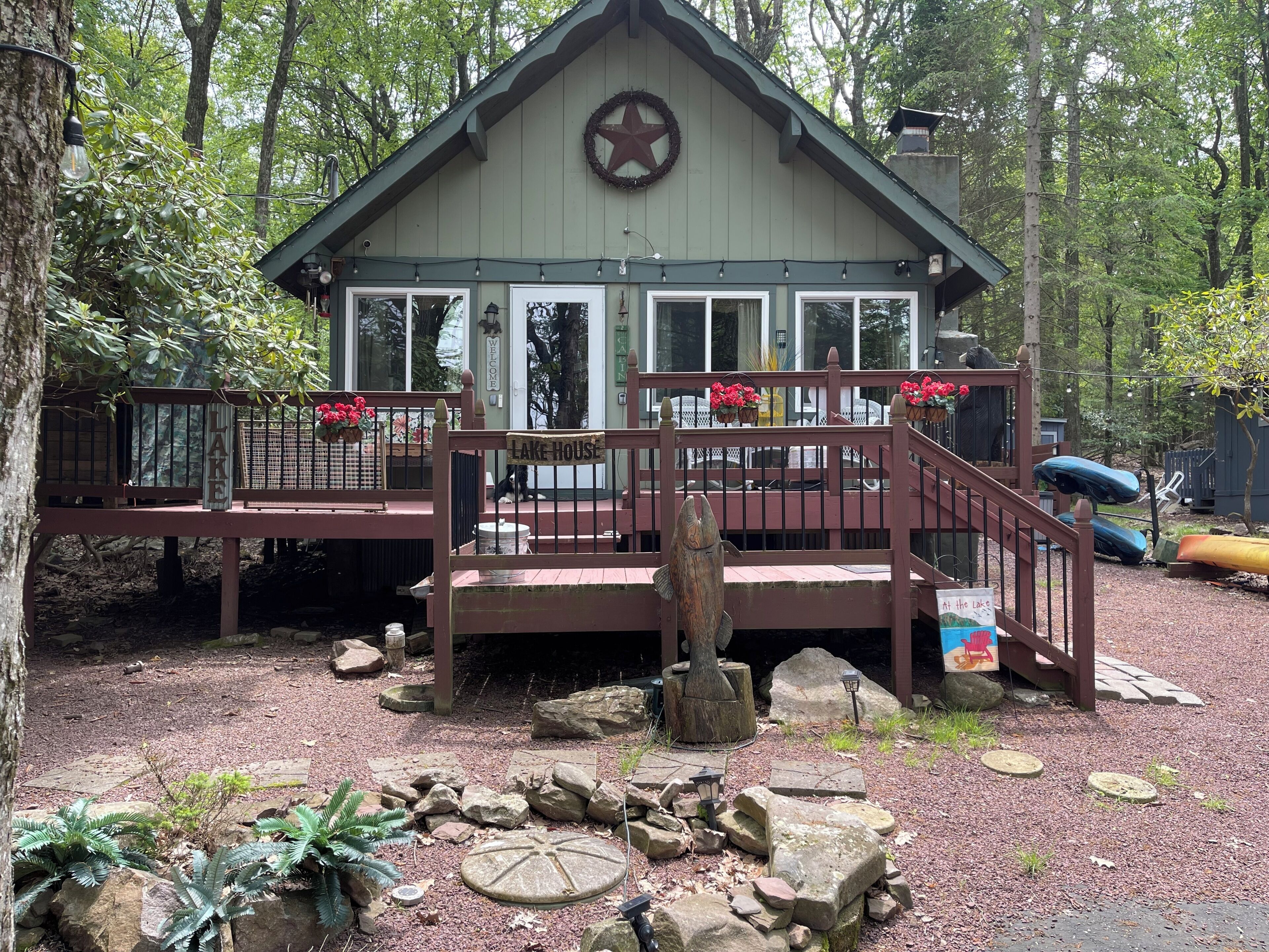 A cabin with a star wreath, a sign reading 'Lake House,' and a dock with a kayak.