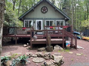 Uma cabana com uma grinalda de estrelas, uma placa com a inscrição 'Lake House' e um píer com um caiaque.