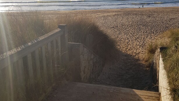 A coastal walkway leading to a beach with a wooden structure on the left and a sandy beach on the right. - Cosy cottage with terrace and private parking (Guidel)