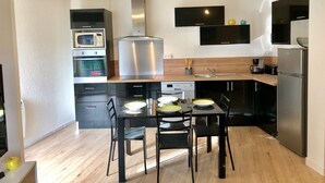 A modern kitchen with a dining area, featuring a microwave, oven, refrigerator, and black cabinets. - Cosy cottage with terrace and private parking (Guidel)