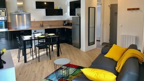 A modern kitchen with a dining area, a sofa with yellow cushions, and a small round table. - Cosy cottage with terrace and private parking (Guidel)