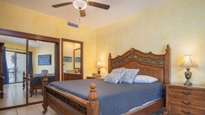 Een slaapkamer met een houten bed, een nachtkastje met een lamp, een dressingkast en een plafondventilator.