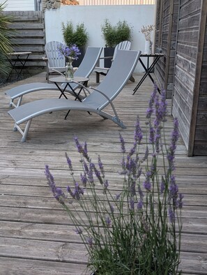 Un espacio al aire libre con sillones de descanso y una mesa, rodeado de plantas y una terraza de madera.