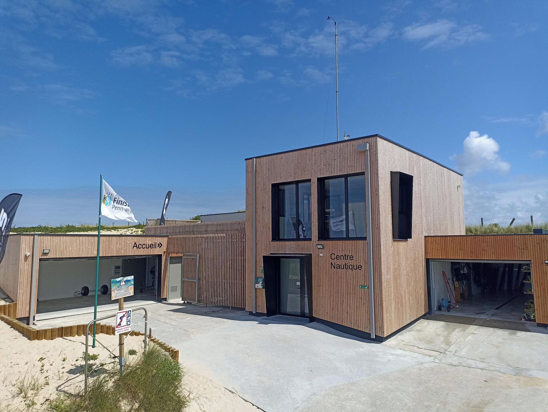Un edificio moderno con fachada de madera, un letrero que dice 'Centre Nautique' y un asta con una bandera.