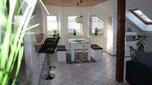 A modern kitchen with a dining area, featuring a bar stool, a table with benches, and a hanging light fixture. - Apartment Kempf Mandelbachtal Saarland (Mandelbachtal)