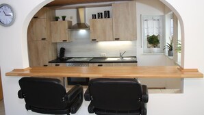 A compact kitchen with wooden cabinets, a built-in stove, and a sink. There is a clock on the wall and a window with a plant. - Apartment Kempf Mandelbachtal Saarland (Mandelbachtal)
