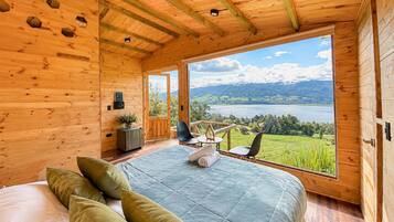 Ein Schlafzimmer in einer Holzhütte mit einem großen Fenster und Blick auf einen See und Berge.