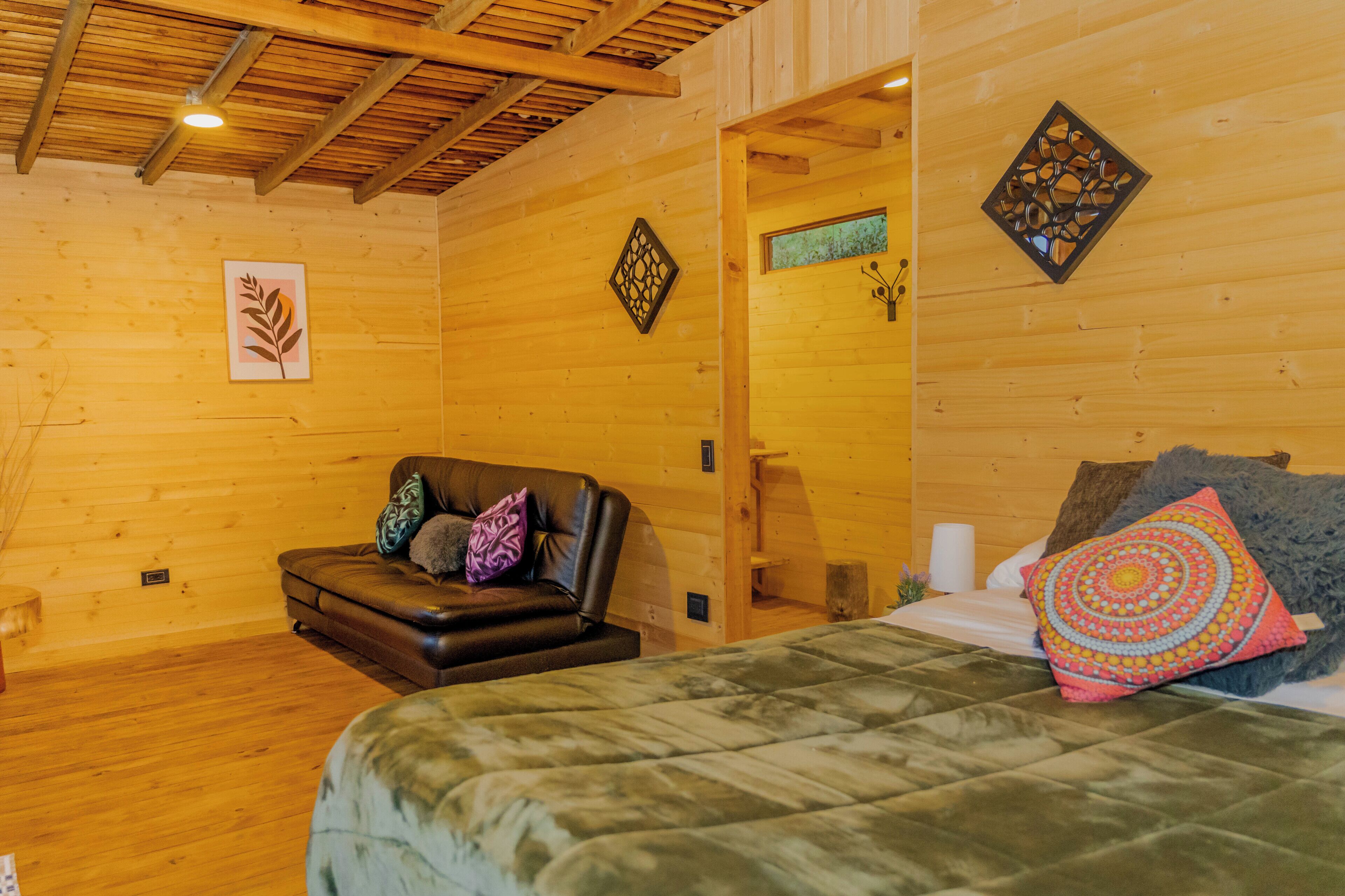 Una camera in una baita di legno con un letto, un divano in pelle e un piccolo tavolo.